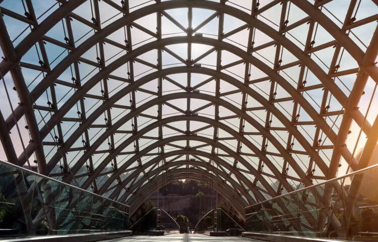 The futuristic cover of a bridge is see-through and shows the sky above.